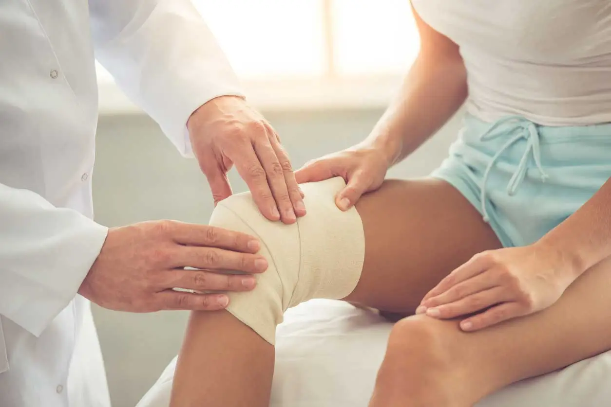 Doctor examining a bandaged knee for wound healing.